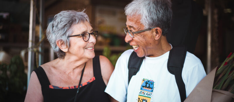 Photo d’un couple âgé souriant, et se tenant par les bras.