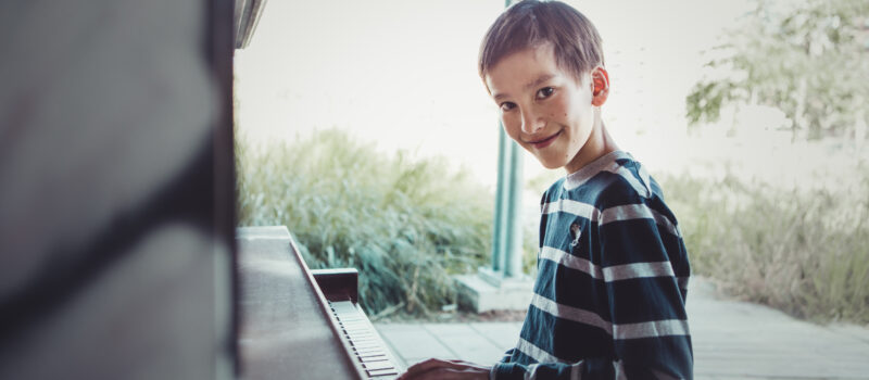 Photo d'un enfant qui joue au piano en souriant à la caméra.