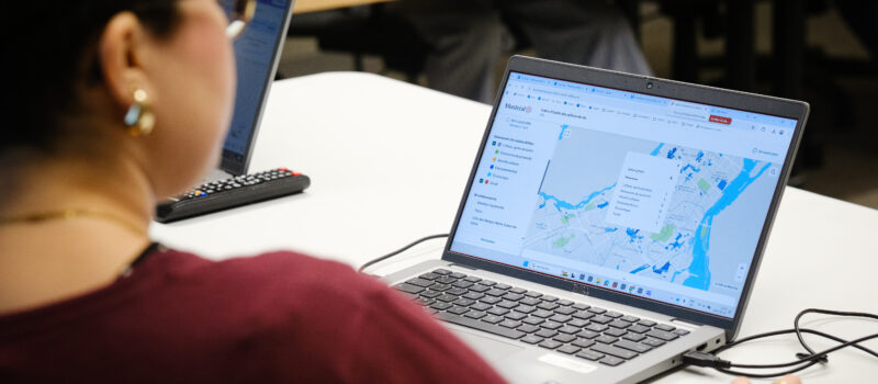 Personne utilisant un ordinateur portable affichant la carte interactive de l’indice d’équité des milieux de vie, qui indique des zones colorées et un menu de navigation. Crédit photo : Sylvie Trépanier